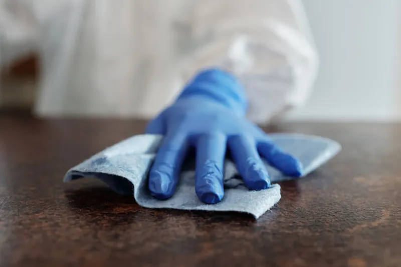 Hand in a blue nitrile glove wiping a dark hard surface with a cloth