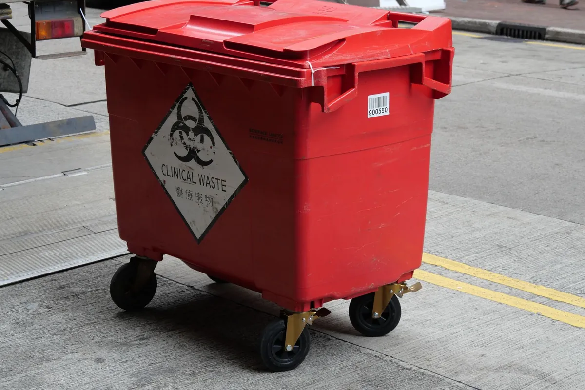 Red wheeled waste bin with a biohazard symbol on a city street