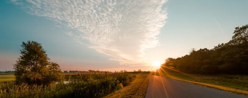 Quiet country road at sunrise with warm light across fields