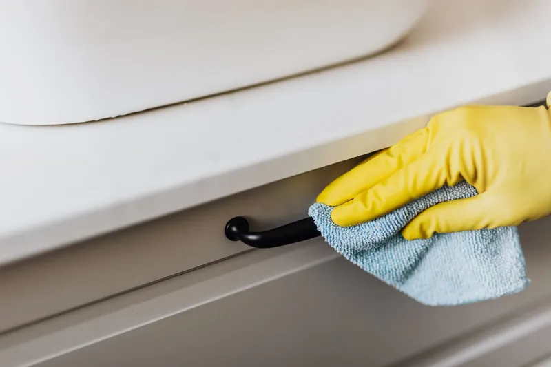 Hand in a yellow glove wiping a cabinet handle with a microfiber cloth